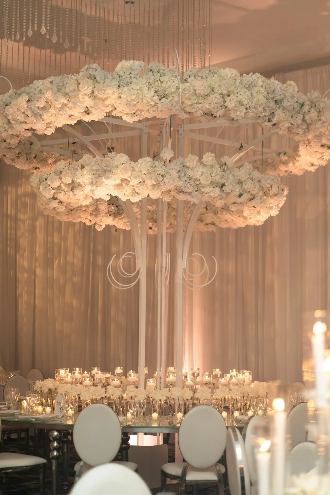 two tier suspended white rose and hydrangea floral chandelier above a candlelit mirror reception table at a Miami luxury wedding