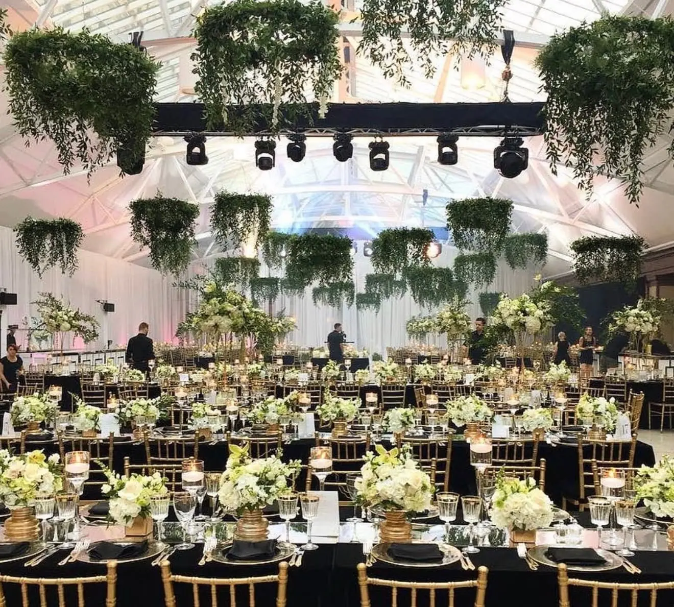 suspended greenery canopy installation over long banquet tables with white hydrangea and rose centerpieces at a Miami tented wedding reception