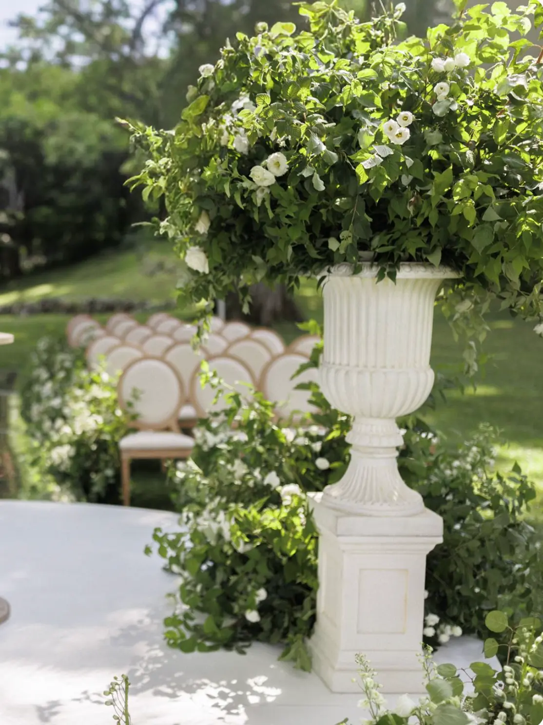 Tall stone urns on pillars with white garden florals framing an outdoor wedding ceremony