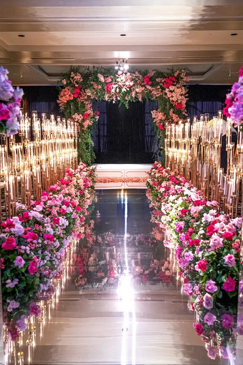 Tall sand-set taper candles in gold holders lining a mirrored aisle with floral arch at a luxury Miami wedding ceremony