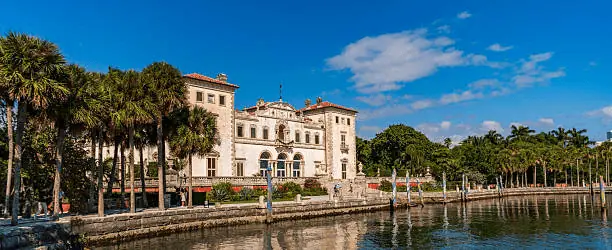The Vizcaya Museum and Gardens villa seen from Biscayne Bay, framed by palm trees under a clear blue sky