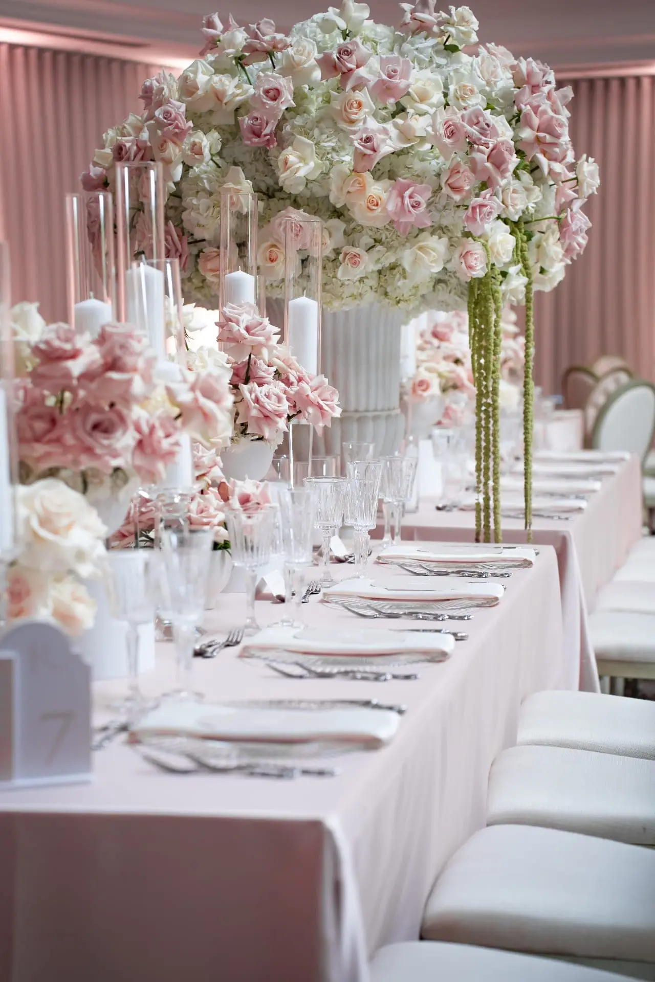 Blush Rose Tall Centerpiece - Towering blush rose and white hydrangea centerpiece with cascading green amaranthus and pillar candles along a long blush reception table by Aura Design Flowers Miami