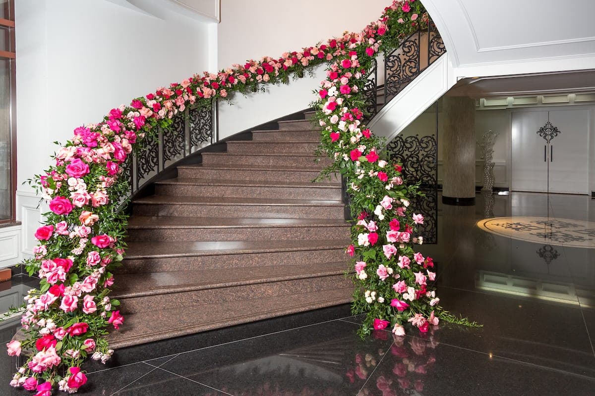 Cascading hot pink and blush rose garland wrapping wrought iron staircase in a marble entryway at luxury Miami wedding