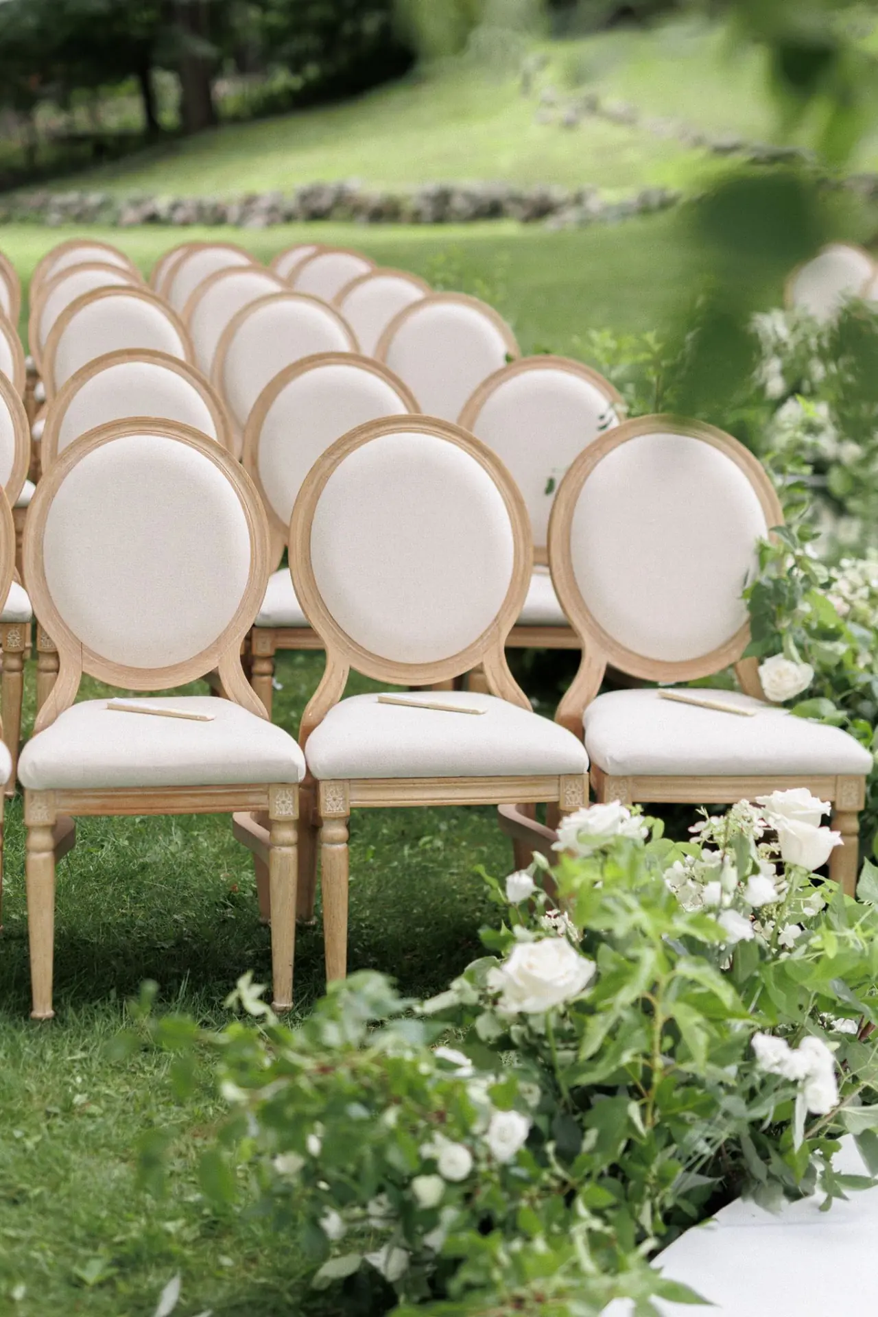 Rows of Louis oval-back ceremony chairs in limewash wood with ivory cushions at a garden wedding