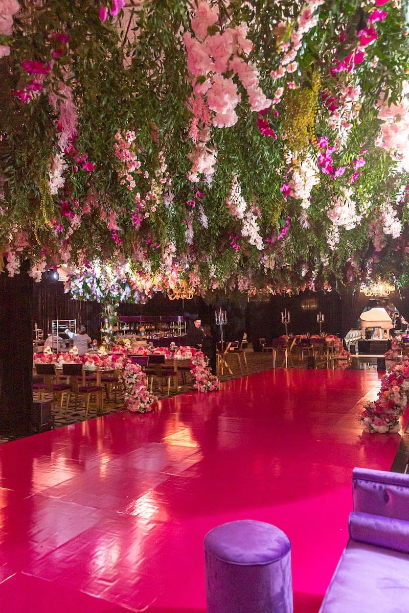Suspended pink rose and greenery canopy above magenta mirrored dance floor with candlelit reception tables at luxury Miami wedding