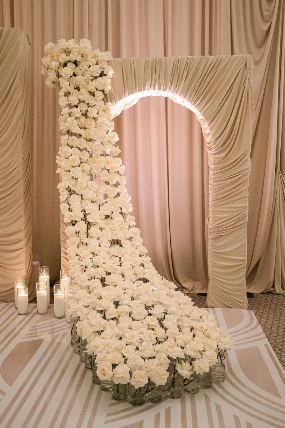 Cascading White Rose Arch - Towering cascade of ivory roses spilling from a champagne draped arch with pillar candles by Aura Design Flowers Miami