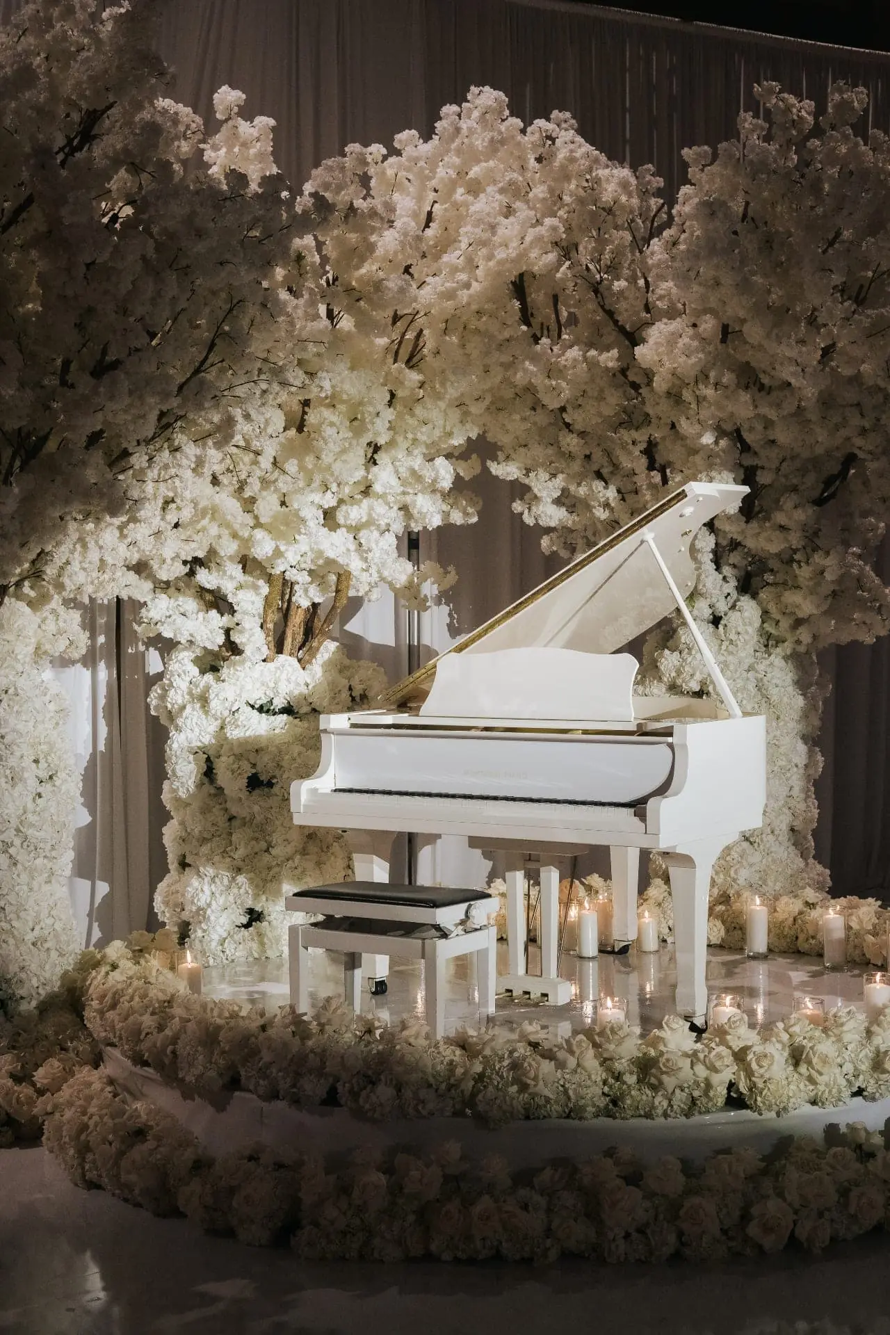 White Piano Blossom Arch - White grand piano framed by towering blossom trees, cascading hydrangeas, and pillar candles by Aura Design Flowers Miami
