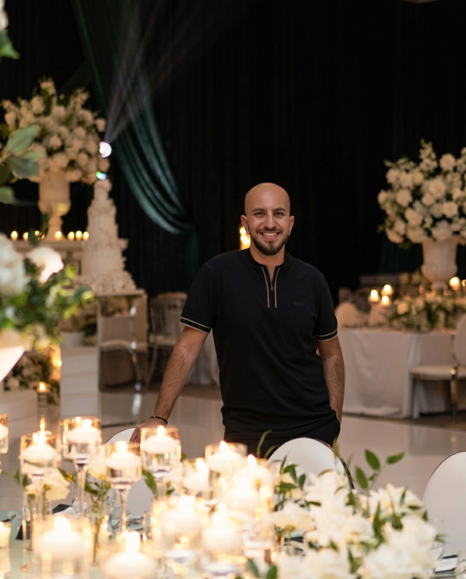 Avo K, in-house luxury event planner at Aura Design Flowers, standing in a candlelit ballroom filled with white florals