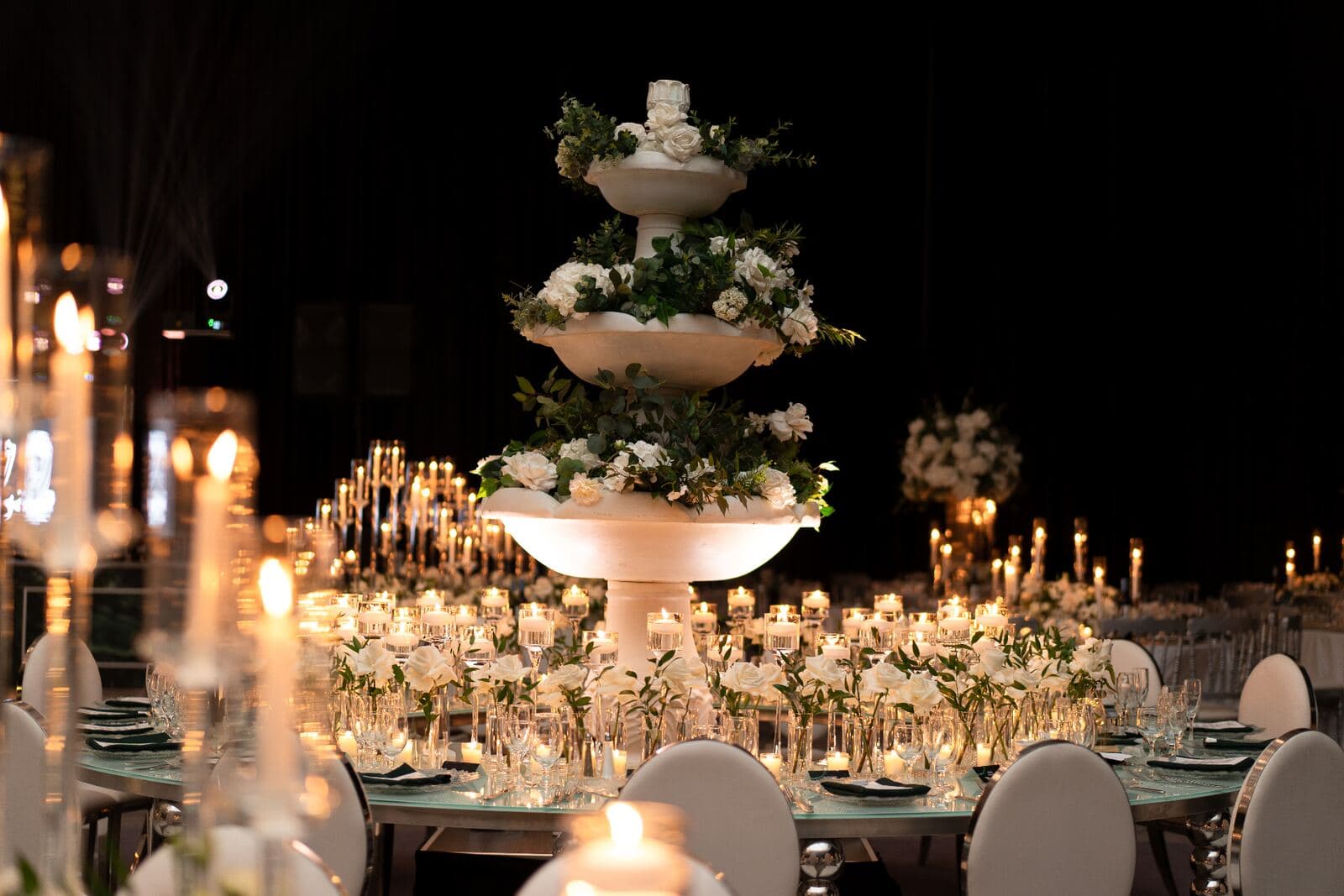 Tiered stone fountain centerpiece overflowing with white roses and greenery surrounded by floating candles at luxury Miami wedding reception