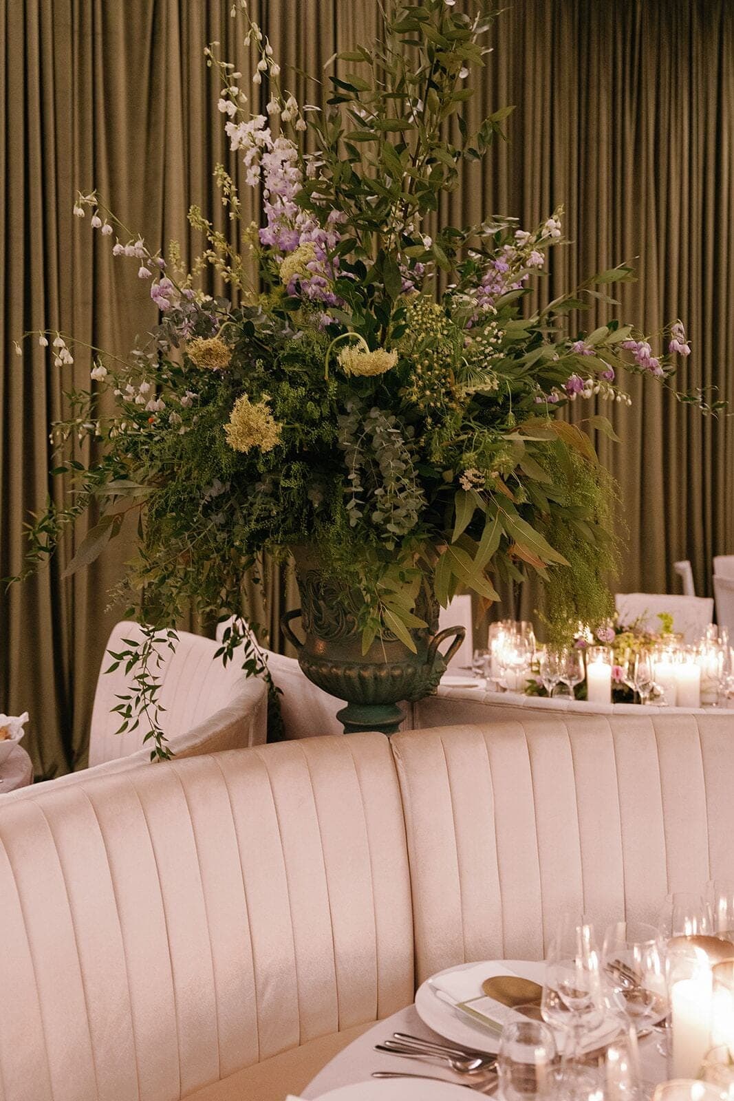 Pedestal Urn Arrangement - Towering wildflower and greenery urn beside an emerald draped reception by Aura Design Flowers Miami