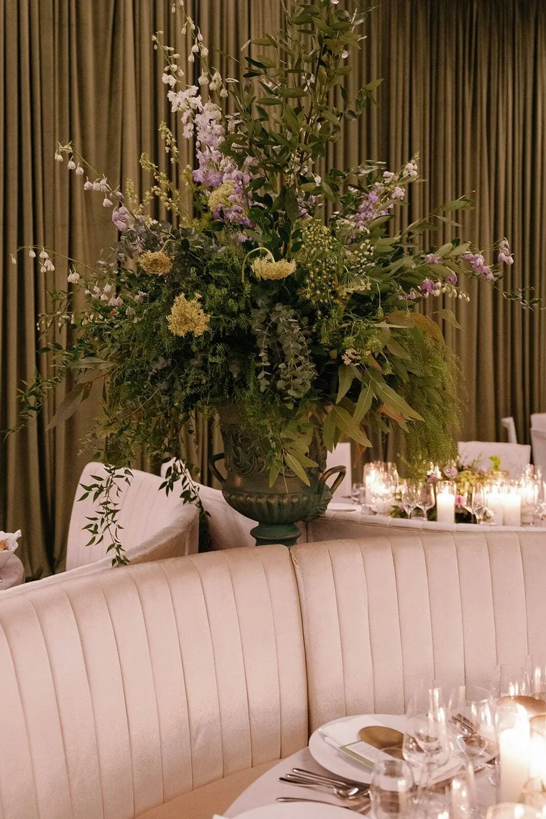 Pedestal Urn Arrangement - Towering wildflower and greenery urn beside an emerald draped reception by Aura Design Flowers Miami
