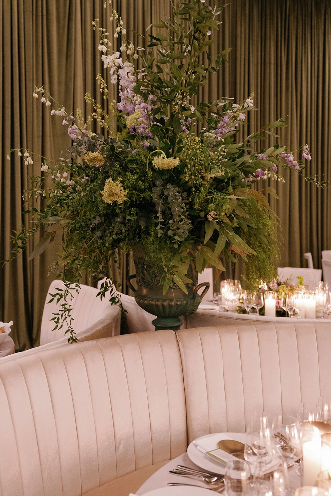 Pedestal Urn Arrangement - Towering wildflower and greenery urn beside an emerald draped reception by Aura Floral Design Miami