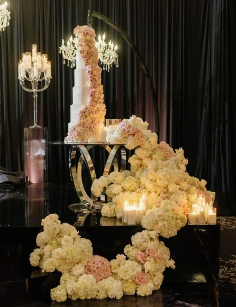Cascading Cake Florals - Tiered wedding cake adorned with roses and lush floral cascade by Aura Design Flowers Miami
