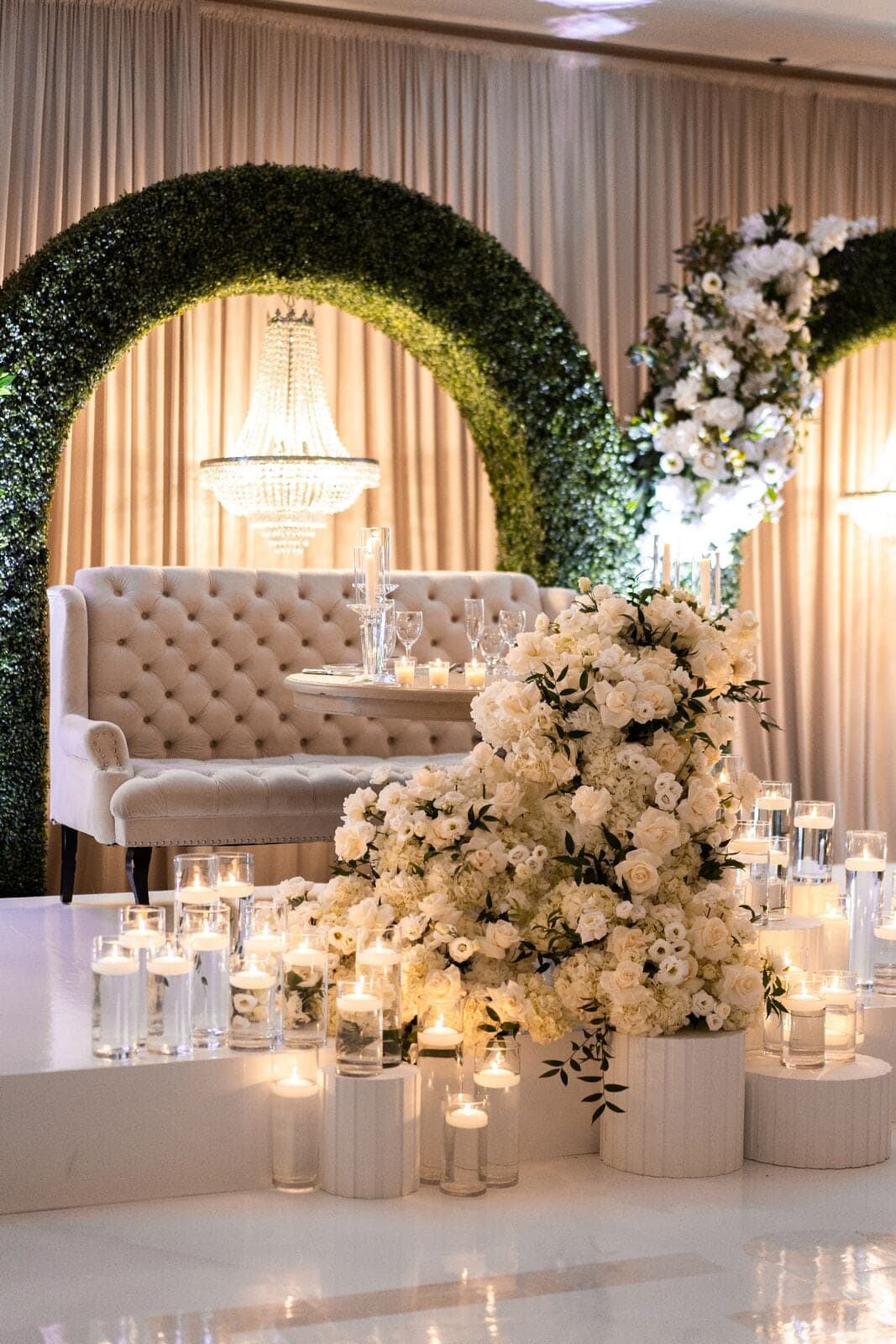 Cascading white rose and hydrangea sweetheart lounge with floating candles, crystal chandelier and boxwood arch at luxury Miami wedding