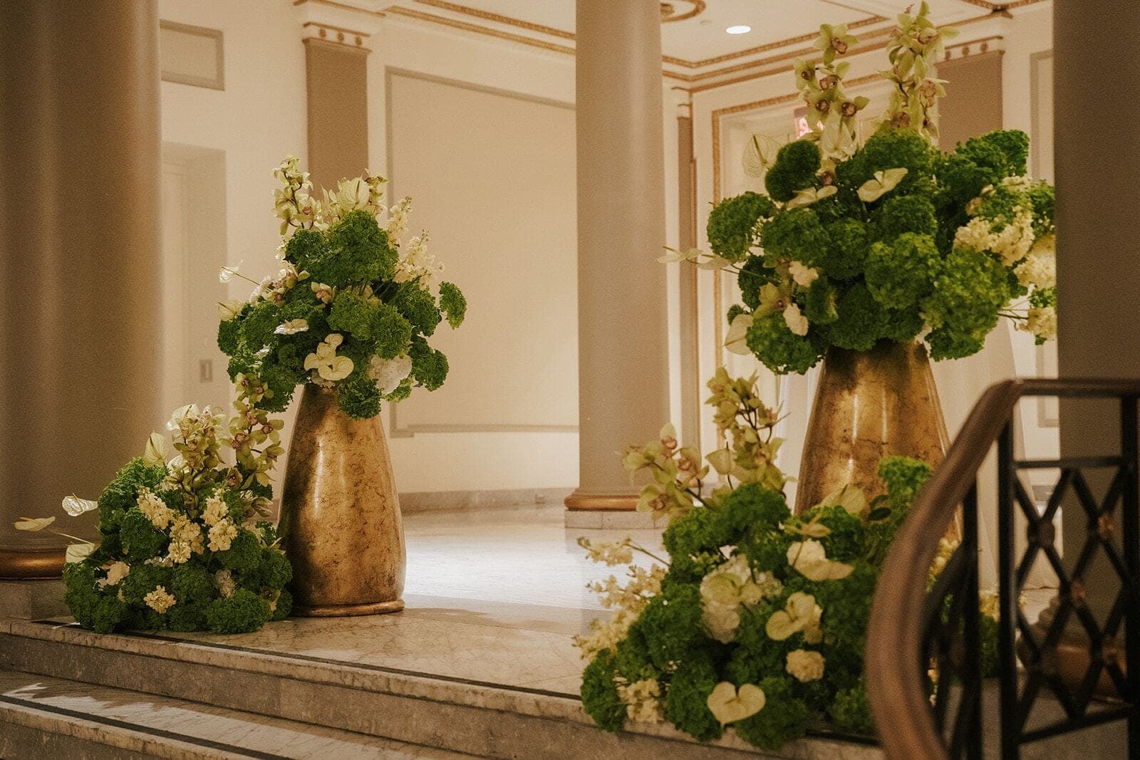 Grand Staircase Vases - Gold vessels overflowing with green and ivory blooms on a marble staircase by Aura Design Flowers Miami