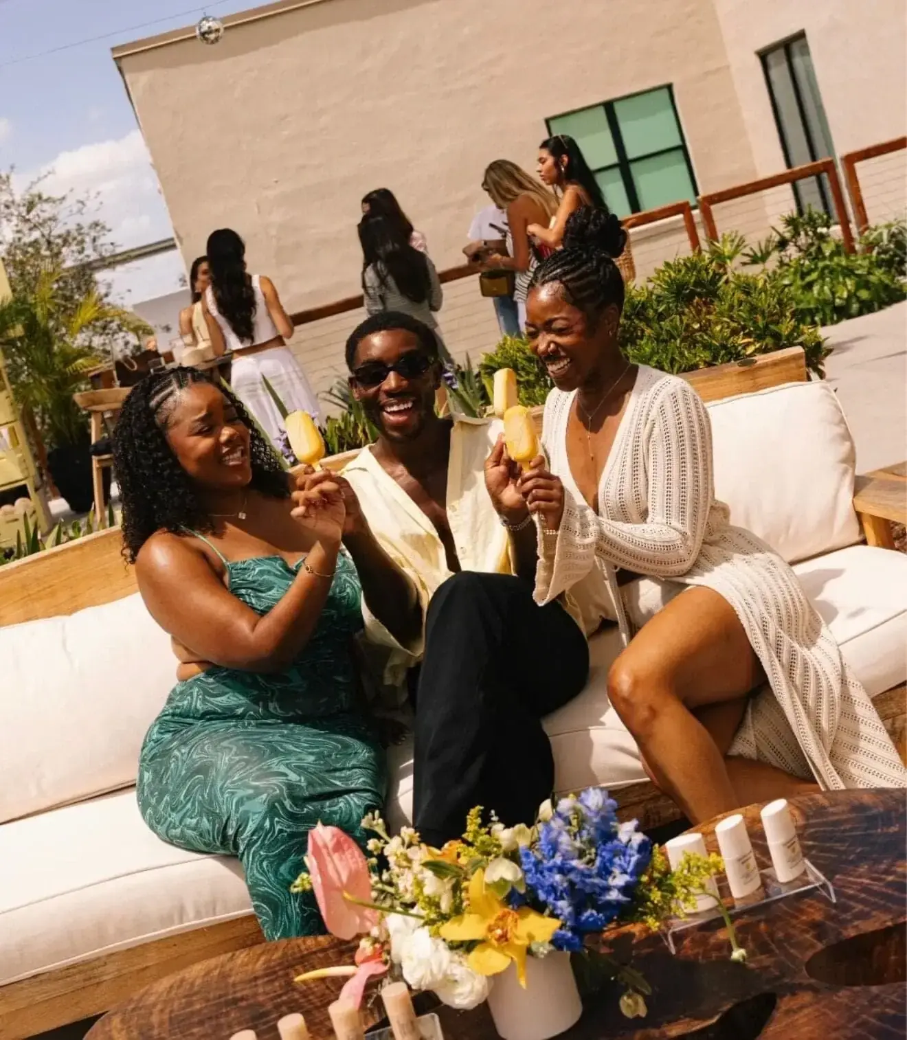 Guests at a Miami beauty brand activation seated around a low floral arrangement with the product lineup staged beside it